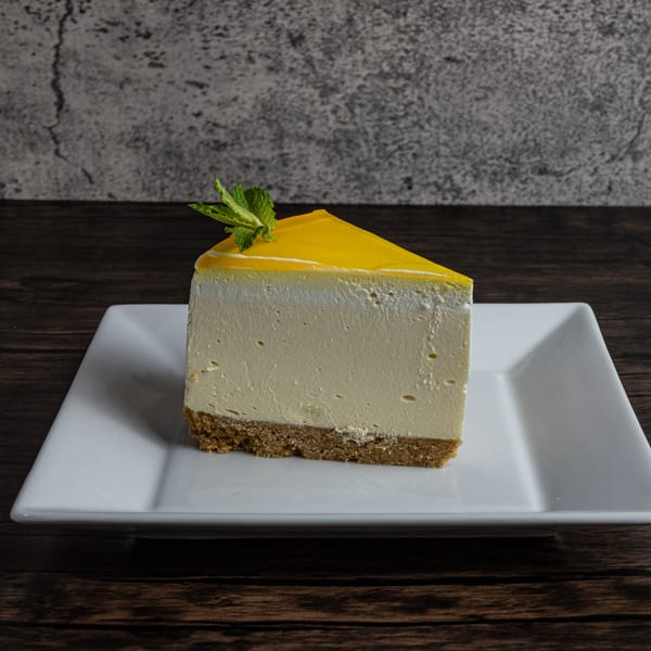 Slice of cheesecake with yellow topping and mint garnish on a white plate.