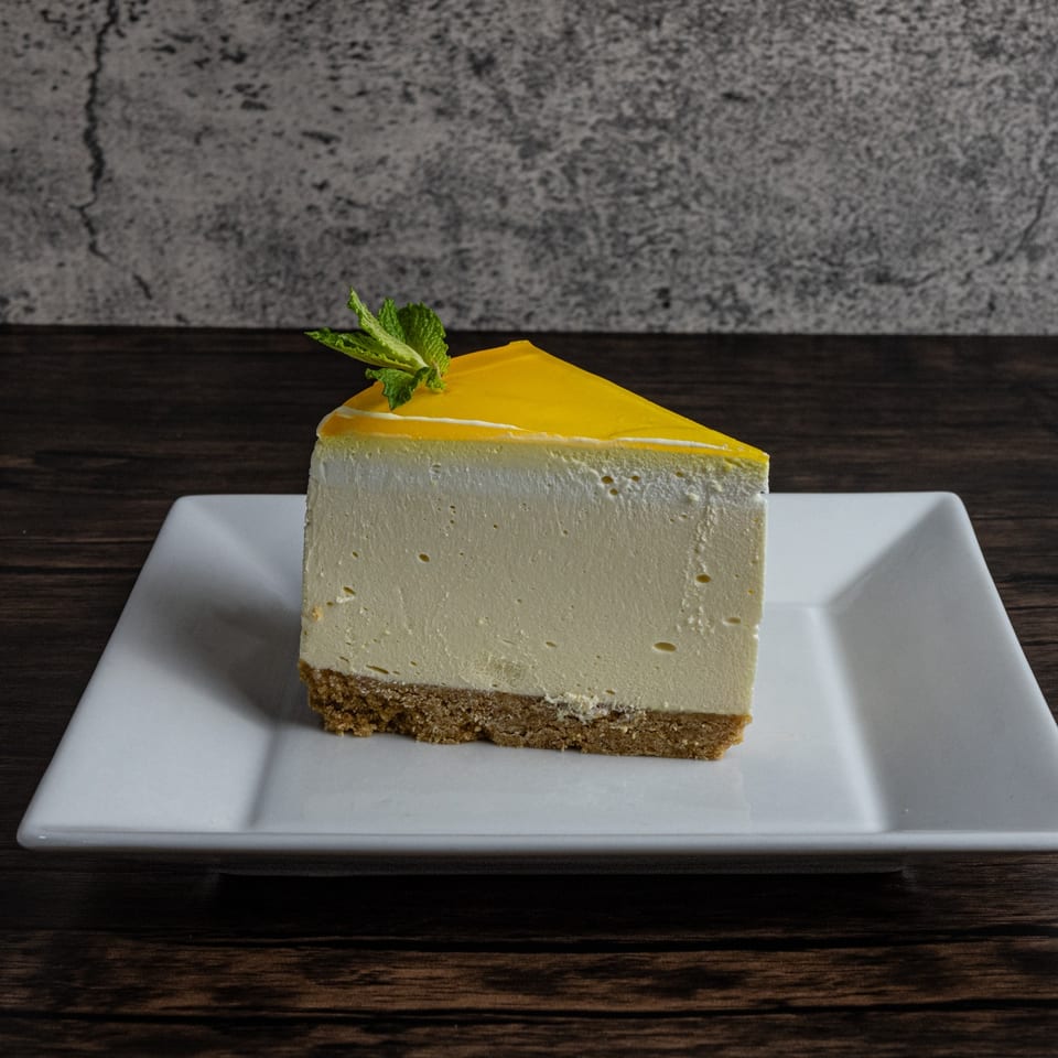 Slice of cheesecake with yellow topping and mint garnish on a white plate.