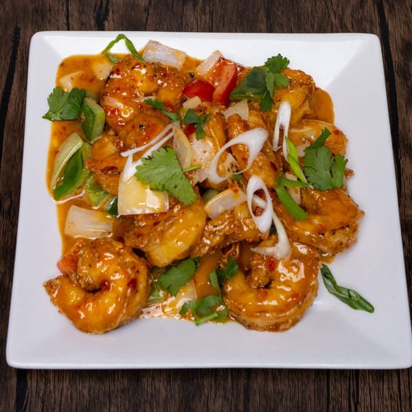 Sweet and sour shrimp with bell peppers, onions, and cilantro on a white rectangular plate.