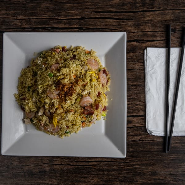 Top-down view of shrimp fried rice on a white square plate with chopsticks and napkin.