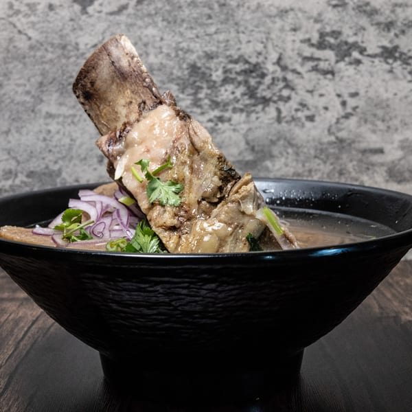A large bone-in short rib in a bowl of broth, garnished with red onions and cilantro.