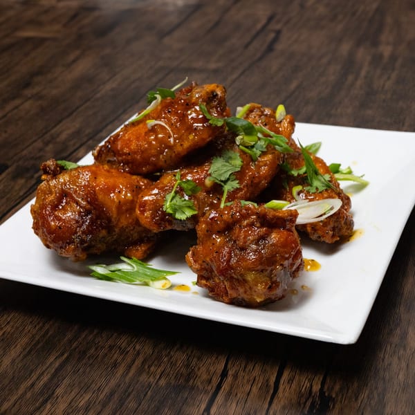 A plate of glistening, saucy chicken wings garnished with fresh cilantro and green onions.